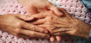 A geriatrician holds the hand of an elderly woman with arthritis.